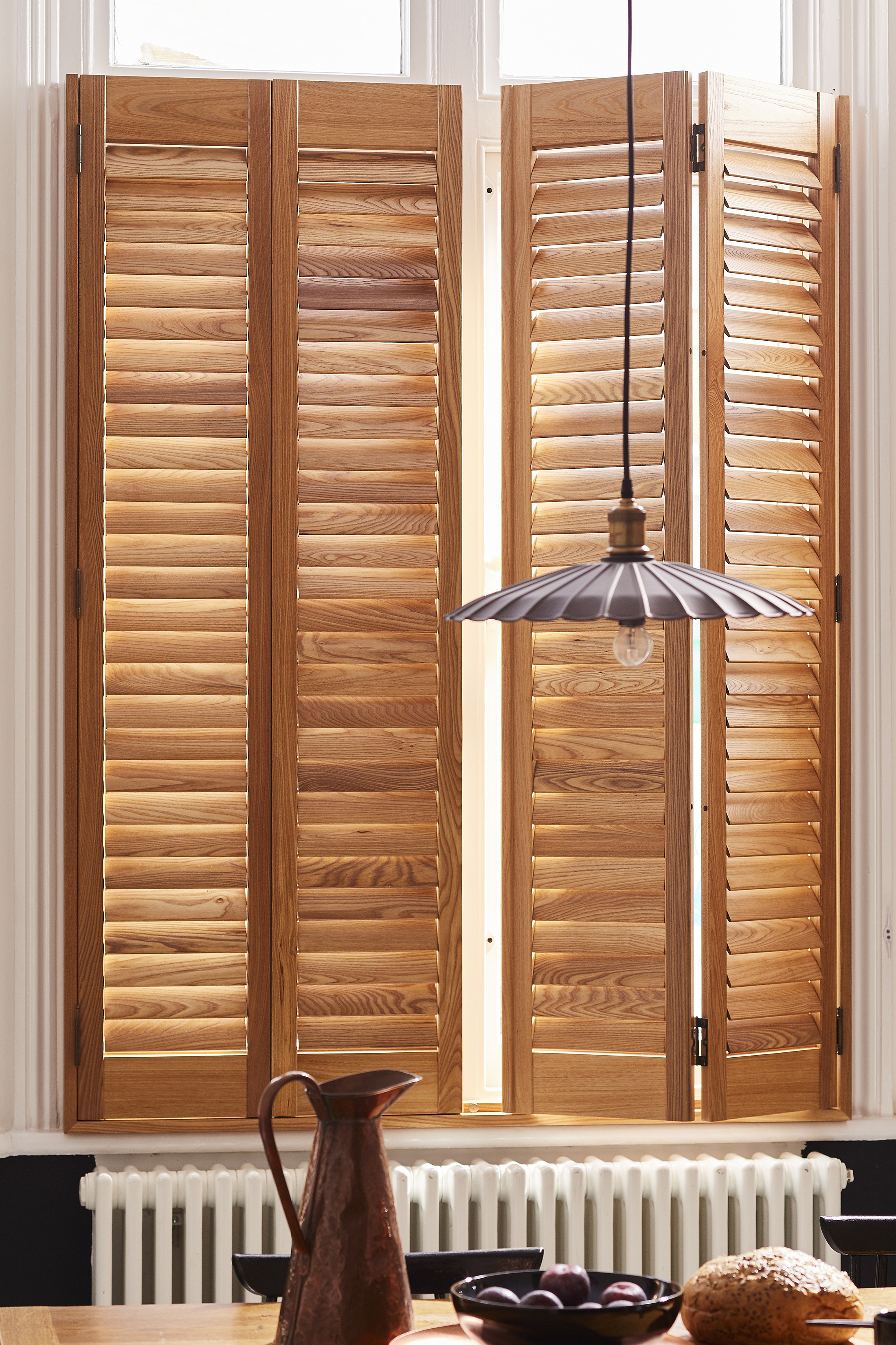 SureFix Shutters Waterlooville – Paulownia, Honey, Dining table, detail, portrait, open Paulownia plantation-style window shutters in honey in a dining room